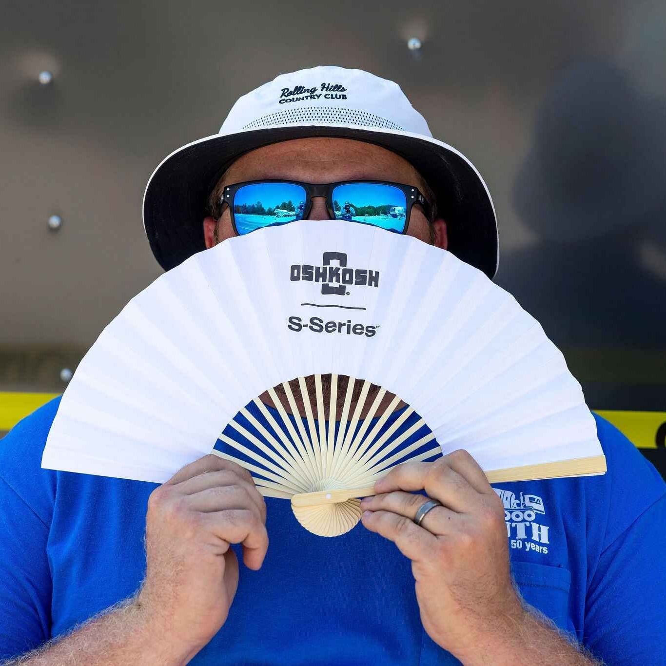 An IRMCA Mixer Driver Championship Volunteer cools off with a branded Oshkosh S-Series portable hand fan.